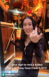 Smiling woman inside a Manhattan trolley making a playful middle-finger gesture, caption reads “your sign to rent a trolley for a birthday food crawl in NYC.”