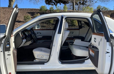White luxury sedan parked outdoors with rear-hinged coach doors open, revealing white leather seats, wood trim and spacious front and rear cabin