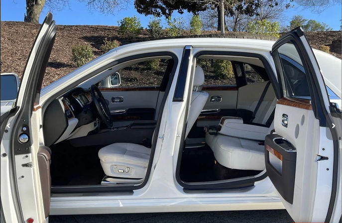 White luxury sedan parked outdoors with rear-hinged coach doors open, revealing white leather seats, wood trim and spacious front and rear cabin