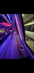 Vibrant purple-and-red LED-lit party bus interior featuring long quilted leather bench seating, built-in cup holders and modern flooring.