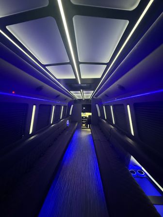 Luxury party bus interior with long side bench seating, glowing white ceiling panels and blue LED accent lights, central aisle and modern flooring for night events.