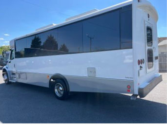 Sleek white passenger shuttle bus with large dark tinted windows and rear entry door parked on a sunny asphalt lot under a blue sky