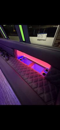 Luxury party bus interior with diamond-stitched leather bench seating and neon pink-purple LED-lit cup holder alcove beneath a window
