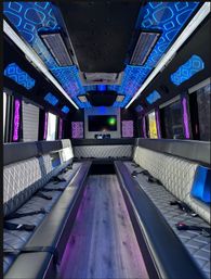 Luxury party bus interior with neon blue and purple LED ceiling patterns, diamond-stitched leather bench seats lining a central aisle, wood-look floor and a flat-screen TV — modern mobile lounge.