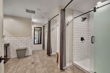 Modern communal shower room with white subway tile, gray curtains, frosted glass door, bench and full-length mirror on a tiled floor