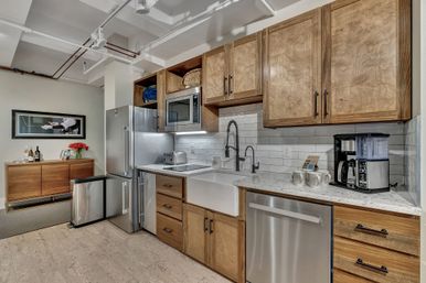 Modern urban loft kitchen with warm wood cabinets, stainless steel appliances, farmhouse sink, subway tile backsplash, marble-look countertops and a coffee station