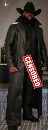 Person wearing a wide-brim black cowboy hat, full beard and long black leather trench coat over a sheer black outfit, red "CENSORED" stamp across the front, standing indoors on a patterned carpet.