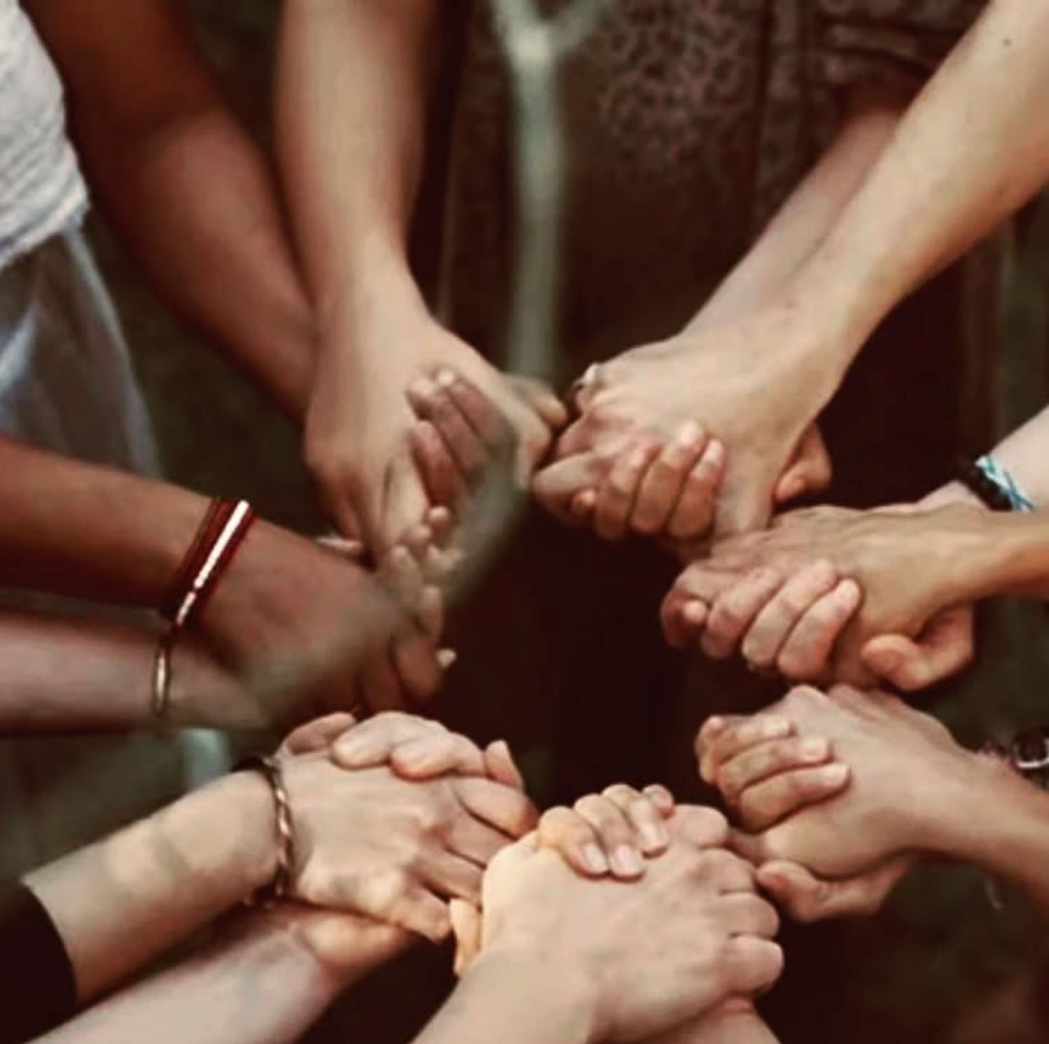 Circle of hands clasped together in a close-knit group, symbolizing unity, support, community, and teamwork.