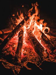 Cozy outdoor campfire at night with stacked burning logs, dancing orange flames and glowing red embers on rocky ground