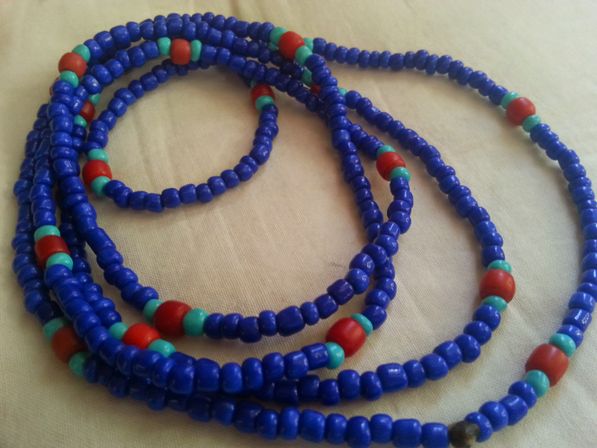 Close-up of coiled multi-strand blue seed bead necklace with red and turquoise accent beads on beige fabric, boho-style jewelry