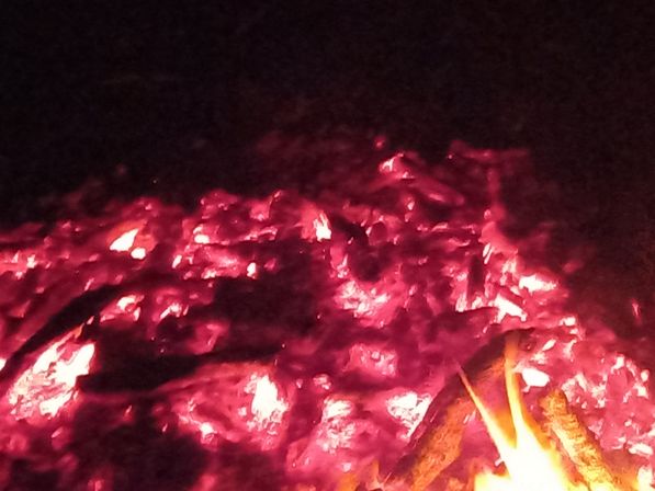 Close-up of glowing red embers and burning logs in a nighttime campfire, hot coals radiating heat