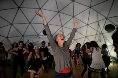Joyful woman with arms raised dancing in a community dance workshop inside a geodesic dome
