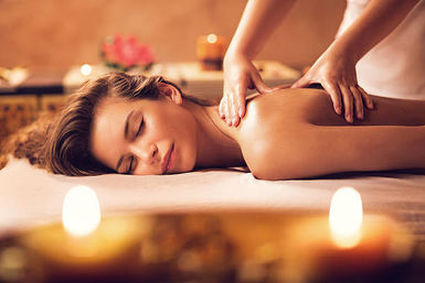 Serene spa scene: woman lying face down enjoying a relaxing shoulder massage on a treatment table with lit aromatherapy candles and warm, soothing lighting