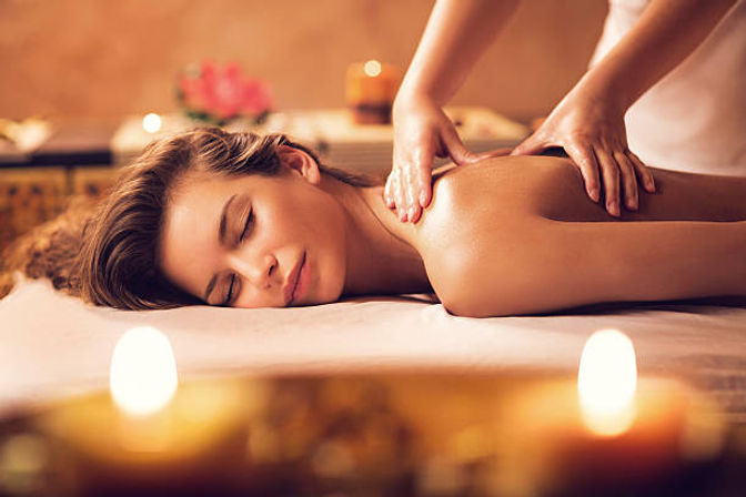 Serene spa scene: woman lying face down enjoying a relaxing shoulder massage on a treatment table with lit aromatherapy candles and warm, soothing lighting