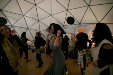 People dancing in a softly lit geodesic dome during a joyful community dance circle and movement workshop.
