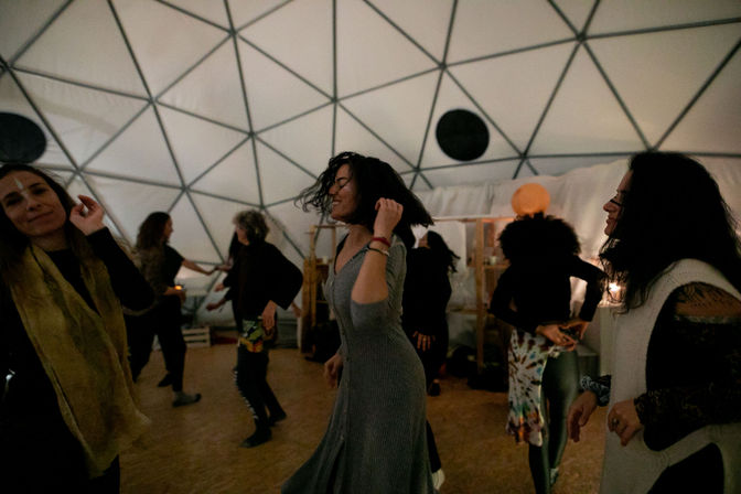 People dancing in a softly lit geodesic dome during a joyful community dance circle and movement workshop.