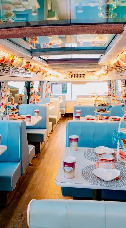 Pastel-blue retro-style party bus interior set for high tea with floral garlands, booth seating and tiered pastry stands