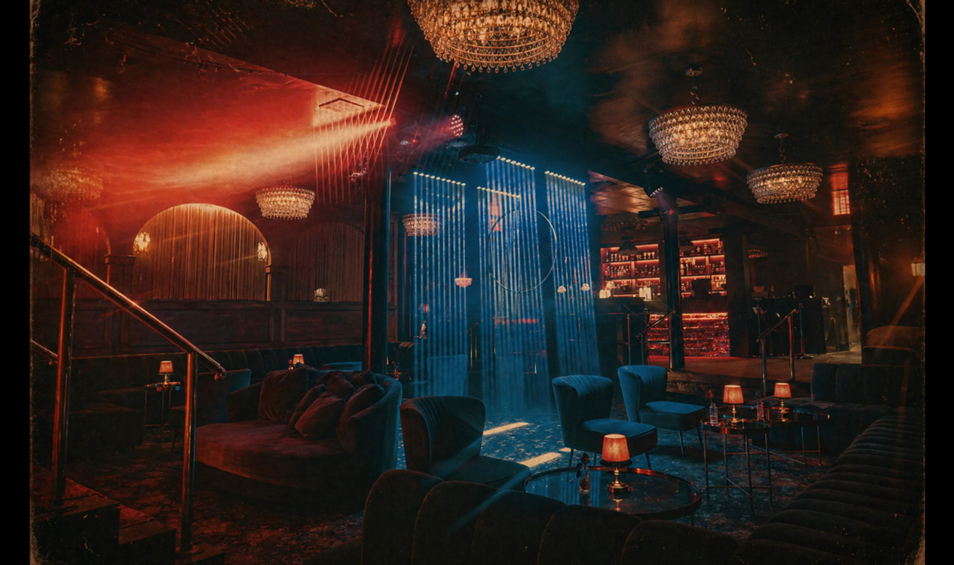 Upscale speakeasy-style lounge interior with plush velvet seating, small table lamps, crystal chandeliers, a glowing backlit bar and vertical blue LED light curtain under moody red and blue ambient lighting.