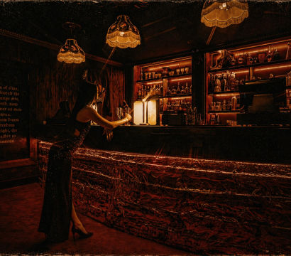 Elegant woman in a black dress at a dim, amber-lit vintage speakeasy bar with backlit liquor shelves and fringe pendant lamps