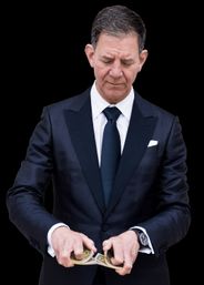 Close-up portrait of a well-dressed man in a dark tuxedo and tie performing a card shuffle with hands mid-motion against a black background.