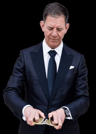 Close-up portrait of a well-dressed man in a dark tuxedo and tie performing a card shuffle with hands mid-motion against a black background.