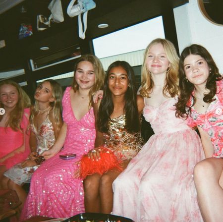 Six teenage friends in colorful party dresses seated together inside a party bus, smiling and posing for a lively group photo during a celebration.