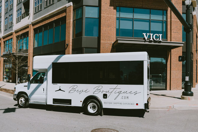 White boutique shuttle parked curbside outside a modern brick storefront with large windows in an urban shopping district