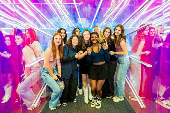 Smiling group of teenage friends posing in a vibrant neon mirror tunnel with pink and blue lights