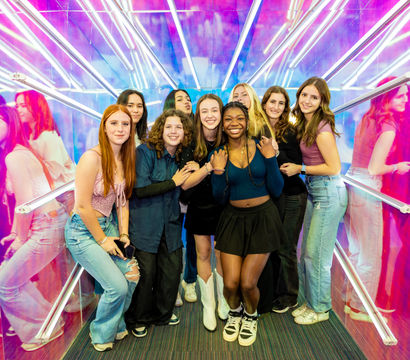 Smiling group of teenage friends posing in a vibrant neon mirror tunnel with pink and blue lights