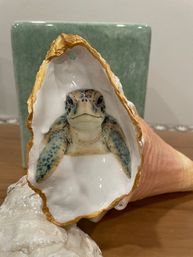 Gold-edged seashell with a realistic painted sea turtle tucked inside, beach-themed coastal decor on a wooden table