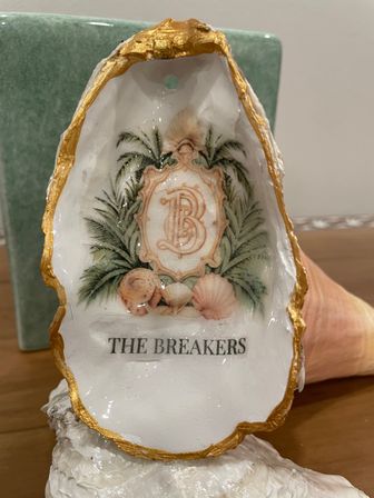Coastal-chic gold-trimmed oyster shell ornament with vintage monogram medallion, palm fronds and seashell illustration on a glossy white interior