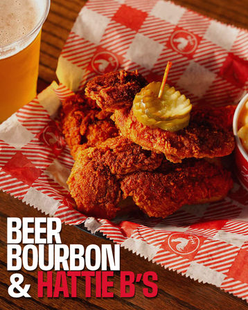 Crispy spicy Southern-style fried chicken tenders piled in a red-check paper-lined basket, topped with pickle slices and served with a cold beer on a wooden table.