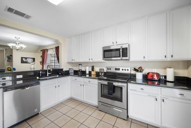 Bright modern white kitchen with stainless-steel appliances, black granite countertops, tiled floor, white cabinets, a red toaster accent and open view to the dining area