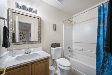 Bright residential bathroom with white bathtub-shower and blue shower curtain, white vanity with mosaic-framed mirror, oak cabinet, chrome fixtures and toilet