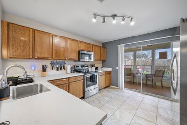 Bright, inviting kitchen with oak cabinets, white quartz countertops, stainless steel stove and microwave, tile floor, and sliding glass door to backyard patio.