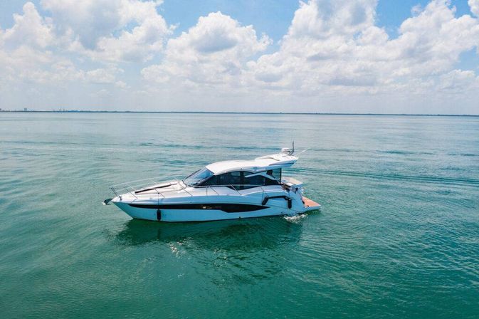 White luxury motor yacht gliding across calm turquoise sea under a bright blue sky with fluffy clouds and a distant horizon