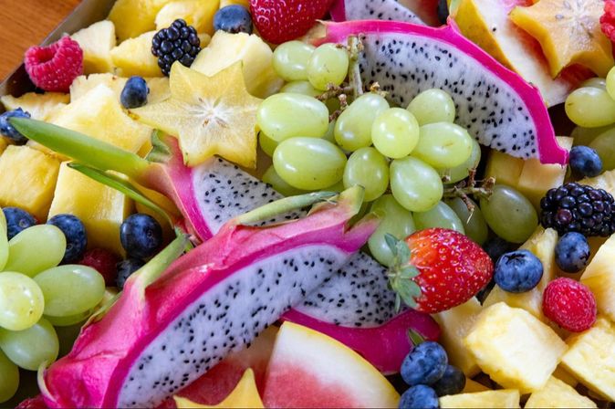 Vibrant tropical fruit platter — sliced dragon fruit, green grapes, pineapple chunks, starfruit, strawberries, blueberries, blackberries and raspberries