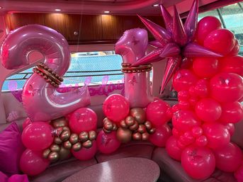 Bright pink balloon arrangement forming the number 21 with metallic gold clusters, spiky accents and butterfly decals inside a boat cabin for a 21st birthday party