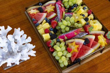 Vibrant tropical fruit platter with watermelon, dragon fruit, green grapes, pineapple, strawberries, blueberries and starfruit on a wooden table.