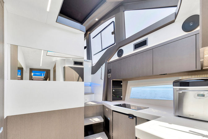Sleek luxury yacht galley with induction cooktop, stainless-steel appliance, wood-tone cabinets, steps up to cockpit and a wide ocean-view window