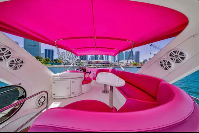 Bright pink-upholstered yacht upper deck with curved seating, small table, and canopy overlooking the Miami waterfront skyline.