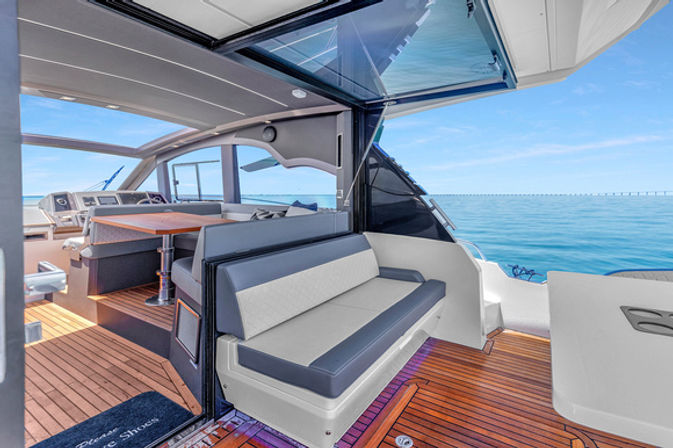 Luxury motor yacht open cockpit with teak deck, cushioned bench seating, dining table and helm, bright ocean horizon