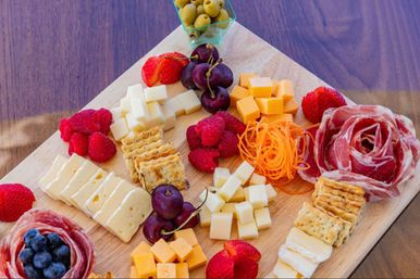Vibrant charcuterie board on a wooden serving board with cubed and sliced cheeses, rolled cured meats, crackers, raspberries, strawberries, cherries, blueberries, olives and carrot curls