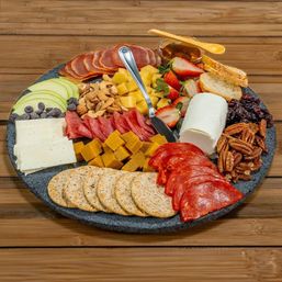 Artisan charcuterie board on a rustic wooden table with a goat cheese log, cubed cheddar, sliced salami and pepperoni, round crackers, apple and strawberry slices, mixed nuts, dried cranberries, chocolate chips, honey and a cheese knife.