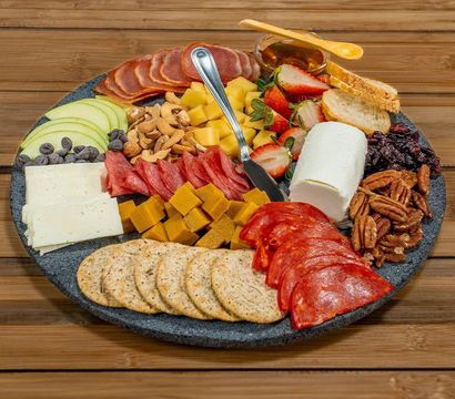 Artisan charcuterie board on a rustic wooden table with a goat cheese log, cubed cheddar, sliced salami and pepperoni, round crackers, apple and strawberry slices, mixed nuts, dried cranberries, chocolate chips, honey and a cheese knife.