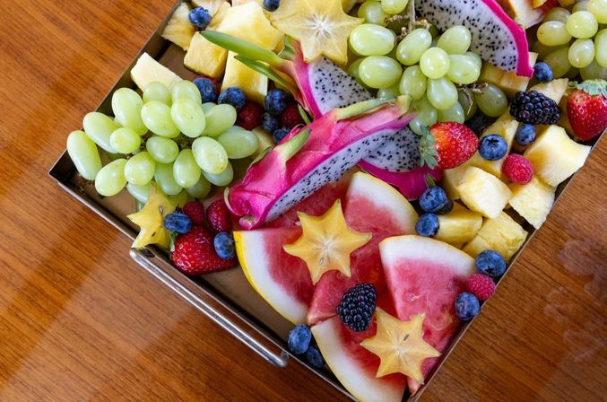 Colorful tropical fruit platter on a wooden table with dragon fruit slices, starfruit stars, watermelon wedges, green grapes, pineapple cubes and mixed berries