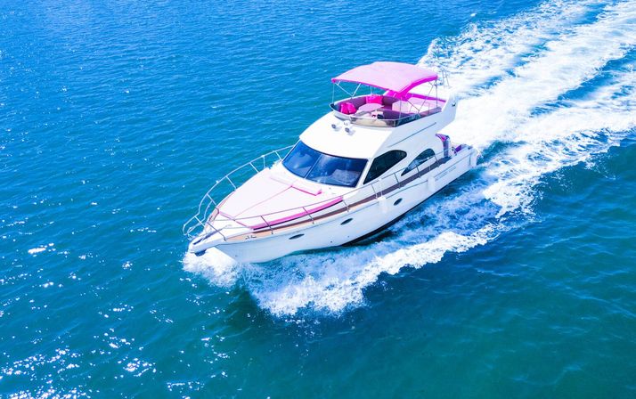 White luxury motor yacht with pink canopy cruising across bright blue water, cutting a foamy wake