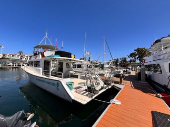 White charter boat moored at a sunny coastal marina next to an orange wooden dock, surrounding boats and a clear blue sky