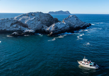 Sightseeing motorboat on deep blue ocean near rugged rocky islands and sea cliffs under a clear sky