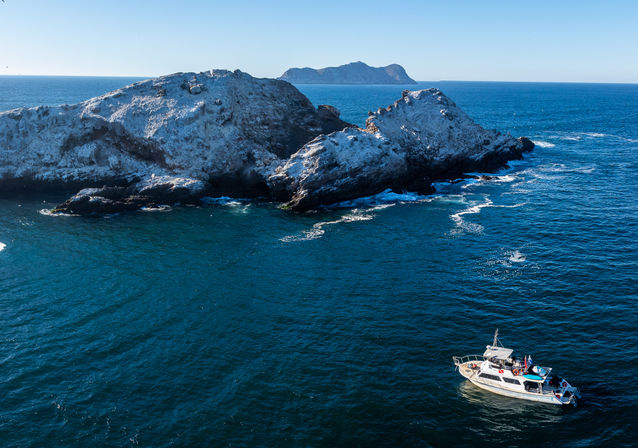 Sightseeing motorboat on deep blue ocean near rugged rocky islands and sea cliffs under a clear sky